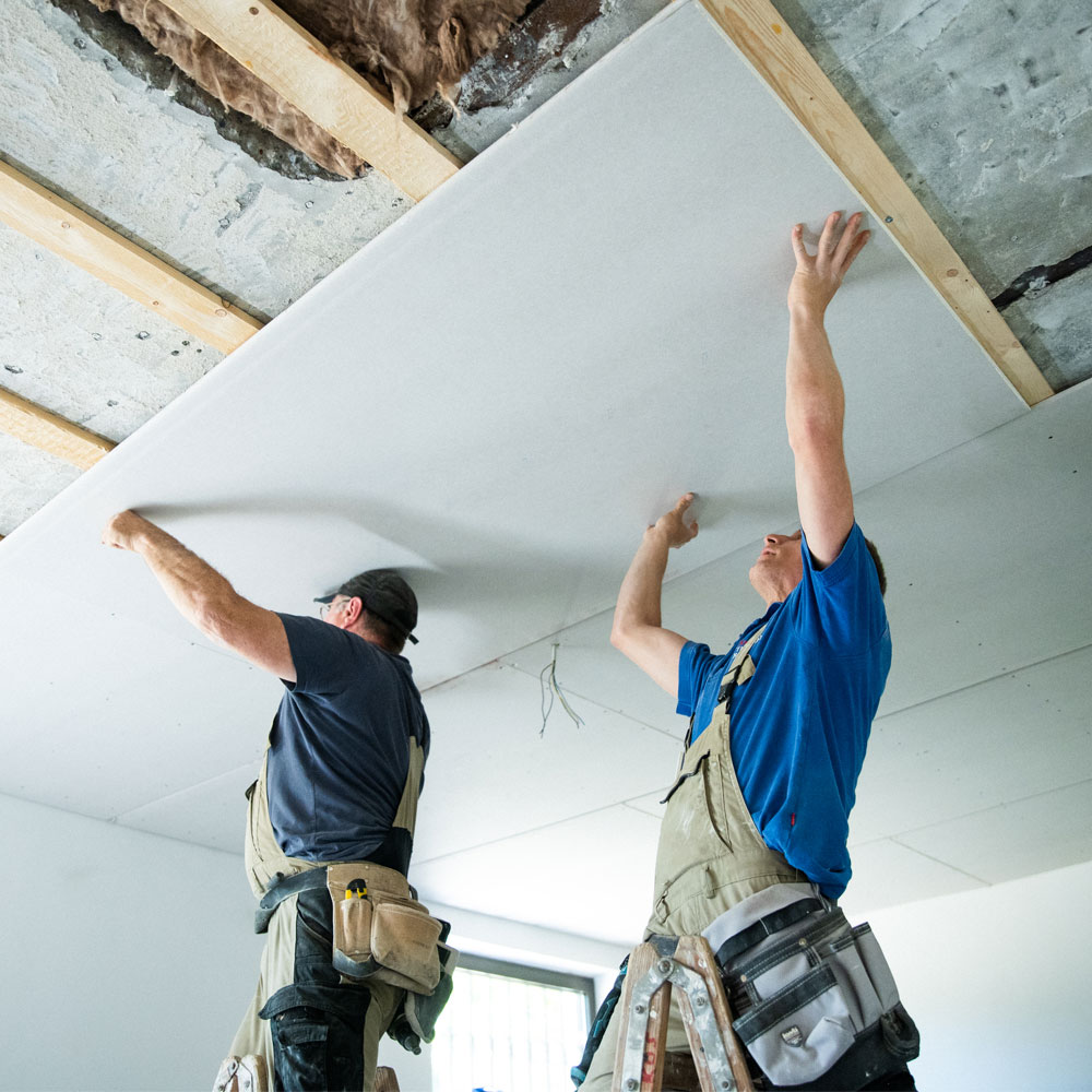 Zwei Handwerker montieren eine Trockenbaudecke als Teil eines professionellen Sanierungsprojekts, mit Fokus auf Teamarbeit und Fachkompetenz.